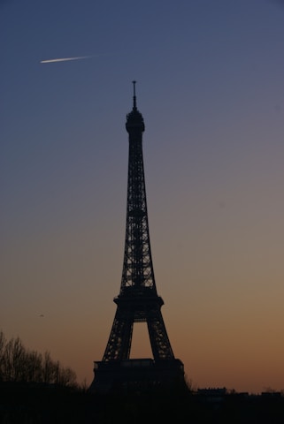 Airplane flying over the Eiffel Tower at sunset.