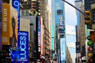 A bustling urban scene featuring tall skyscrapers adorned with bright, colorful billboards and digital advertisements. The street is lined with signs and electronic displays, showcasing various messages and images. The atmosphere is vibrant and lively, embodying the energy of a busy city intersection.