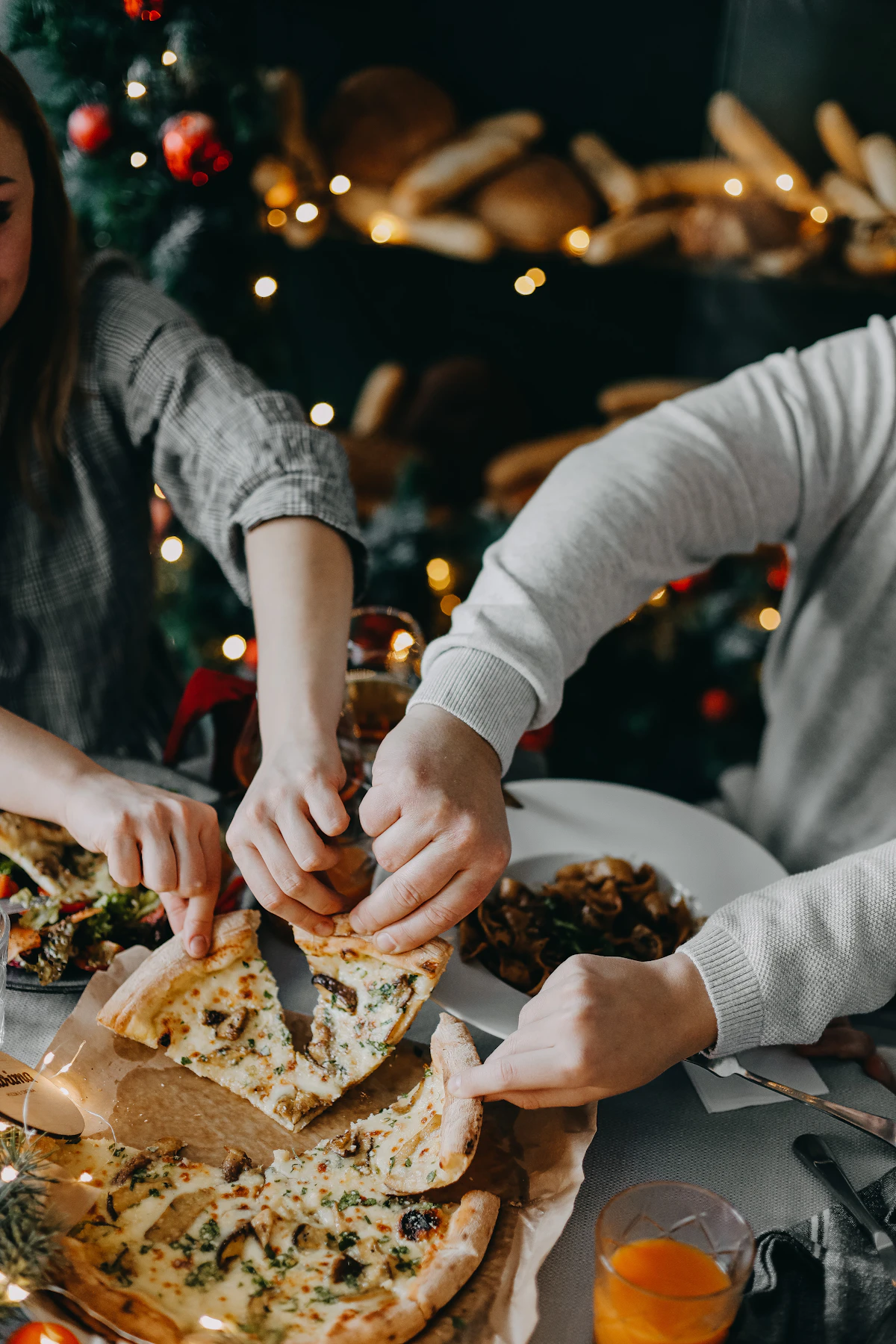 Hands taking slices from a shared board at a lit table after dark