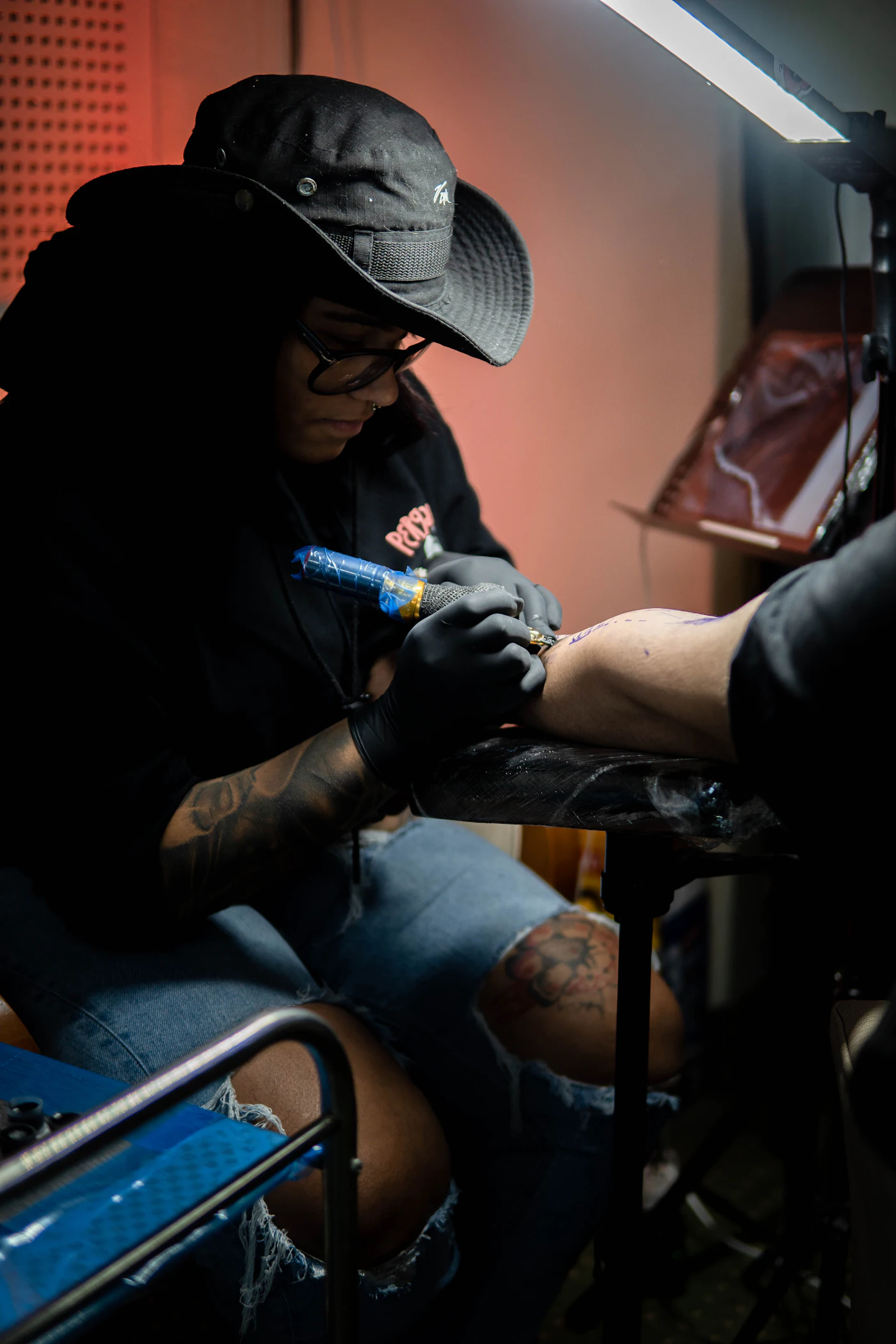 Tatuadora de luvas pretas começando a sessão no braço do cliente
