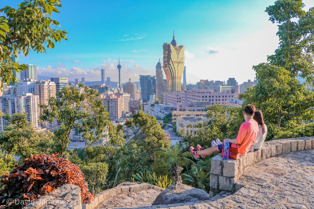 a man sitting on a rock ledge overlooking a city