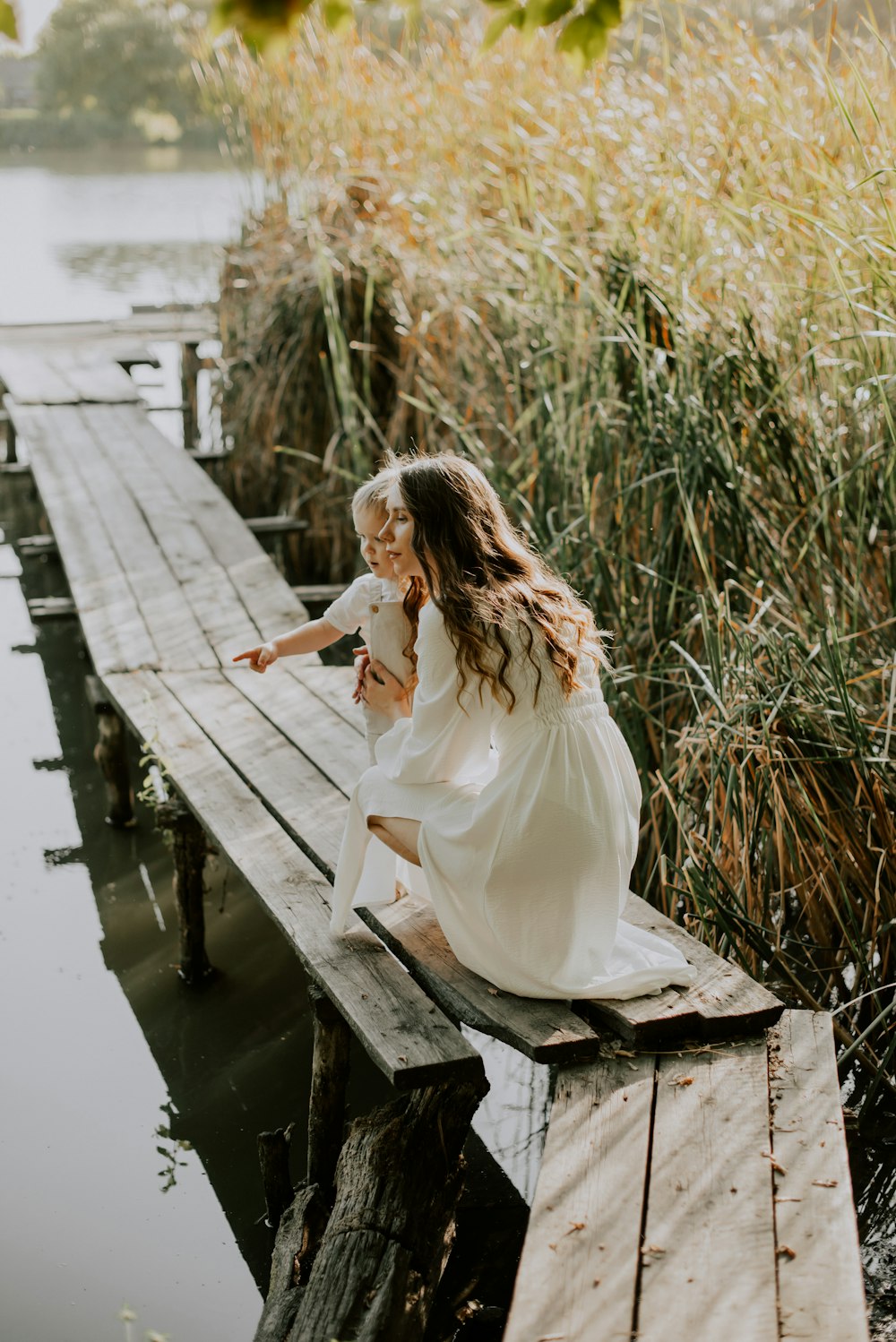 a person in a white dress sitting on a wooden bench in a marsh