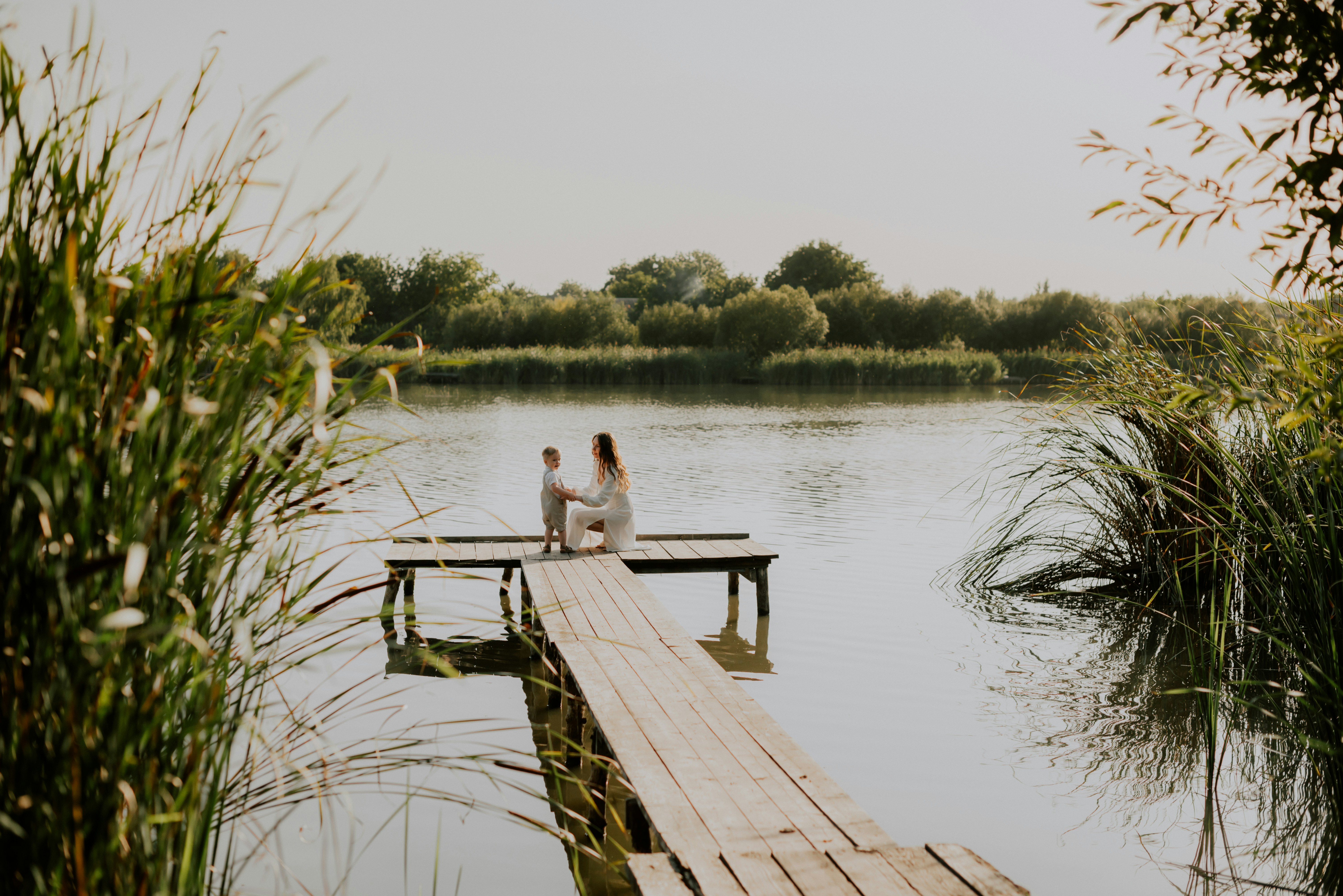 Mom sitting by a lake with her toddler son, sharing a quiet bonding moment and encouraging early communication through connection