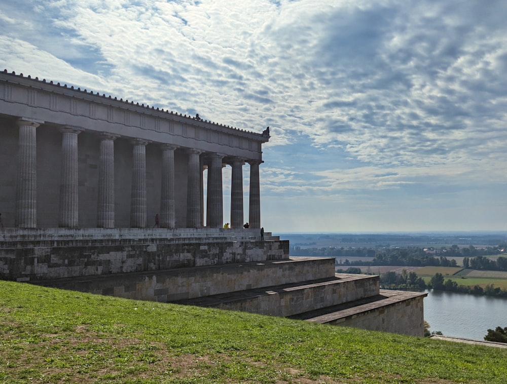 a building with columns and a body of water in the background