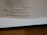 A page from a book is open, showing text from the Proverbs of Solomon. It includes a verse about the joy and grief brought by a wise or foolish son to his parents. The page is partially blurred and the book is lying on a wooden surface.