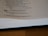 A page from a book is open, showing text from the Proverbs of Solomon. It includes a verse about the joy and grief brought by a wise or foolish son to his parents. The page is partially blurred and the book is lying on a wooden surface.