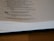 A page from a book is open, showing text from the Proverbs of Solomon. It includes a verse about the joy and grief brought by a wise or foolish son to his parents. The page is partially blurred and the book is lying on a wooden surface.