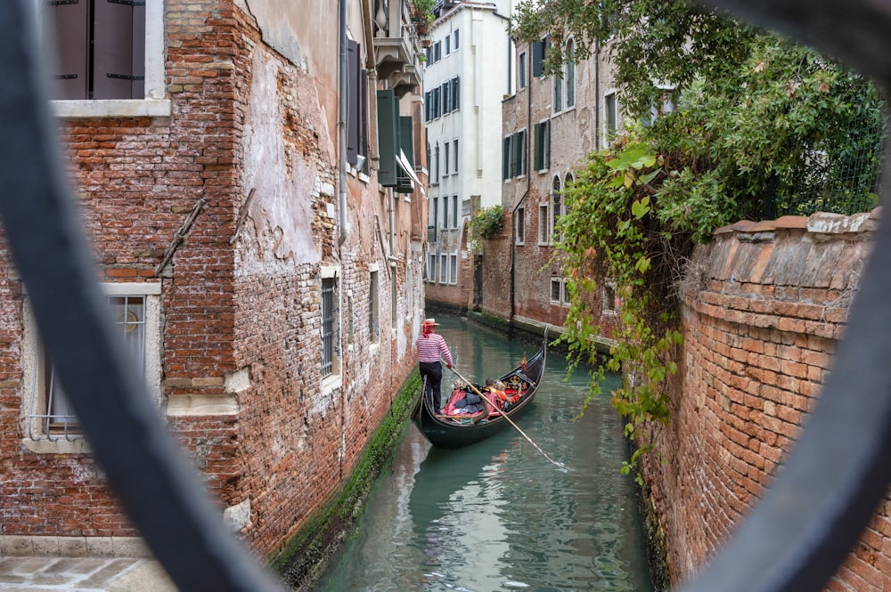 a person on a boat in a canal between brick buildings