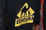 A black garment featuring a triangular yellow logo with the silhouette of a camel and a person. The text 'Essaouira Maroc' is displayed prominently in bold letters below the figures.
