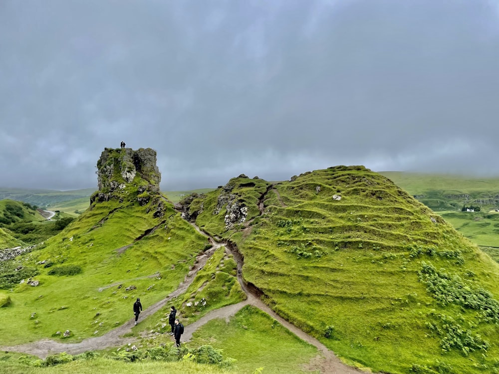 people walking on a path in a grassy area with a stone structure on top of it