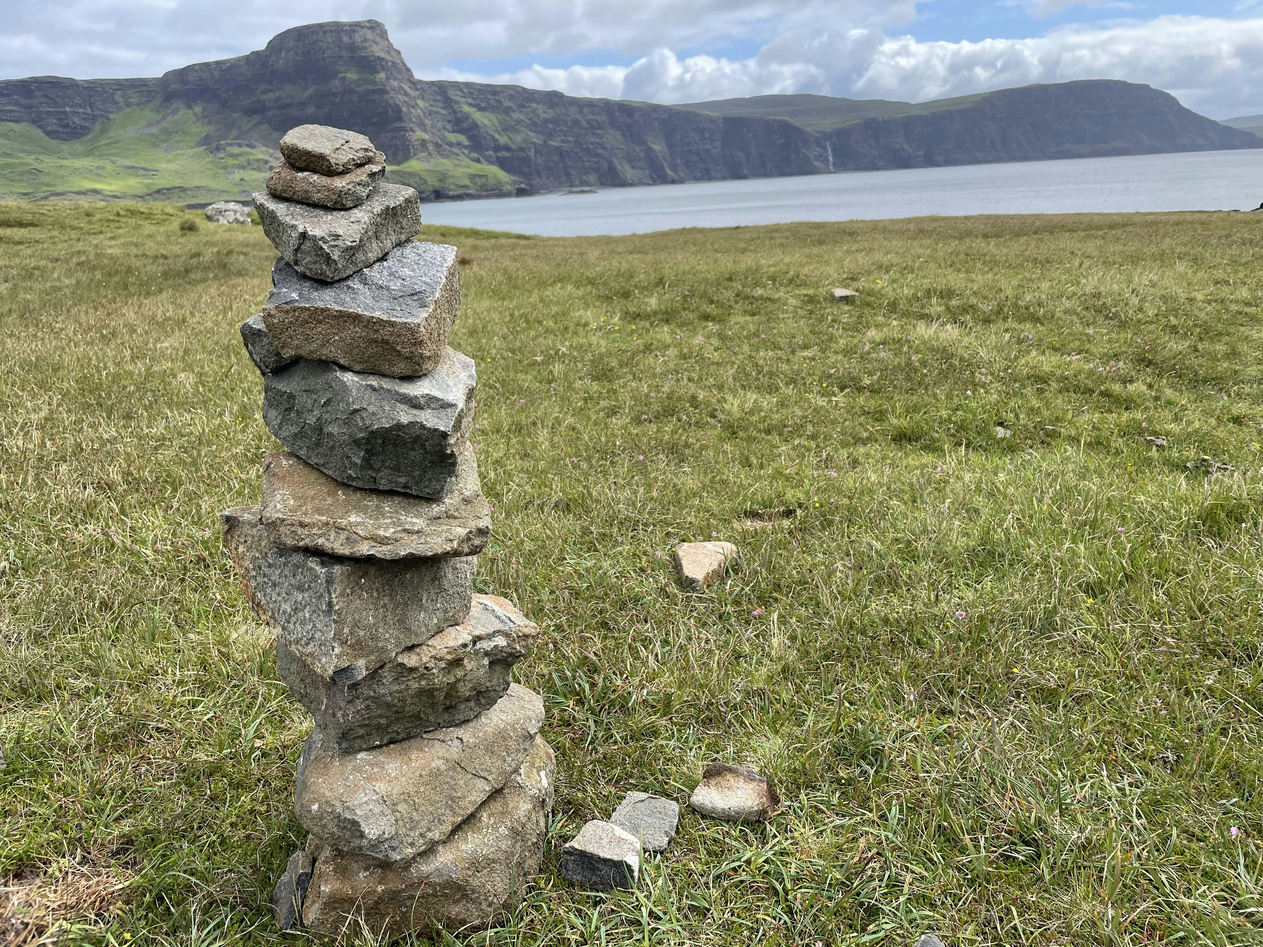 a stack of stones in a grassy field with water in the background