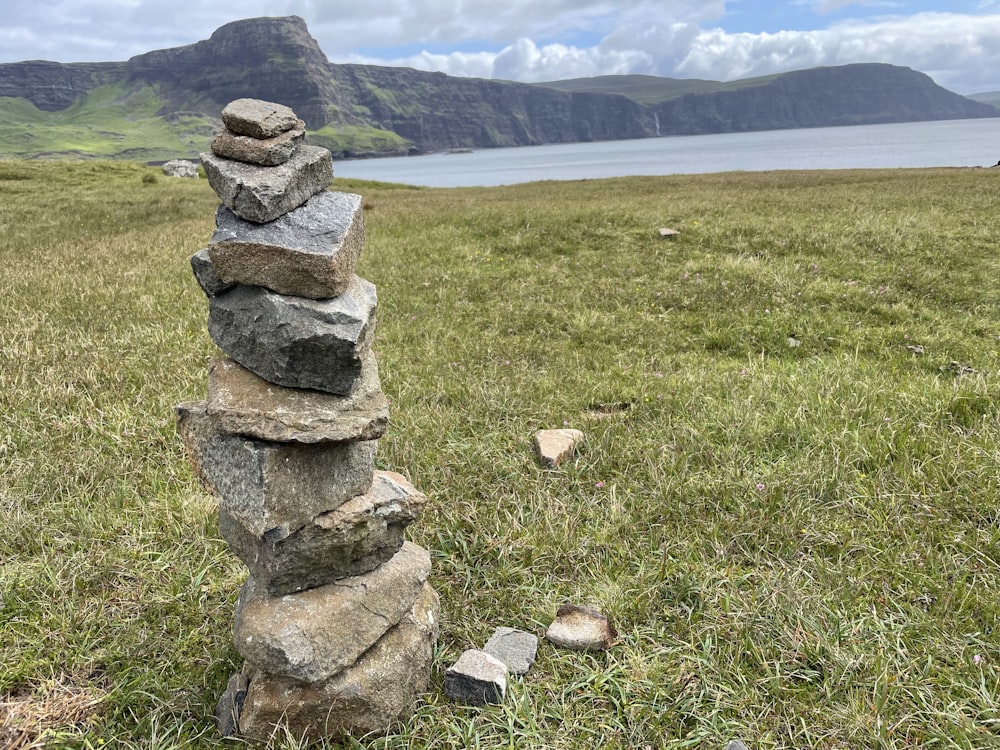 a stack of stones in a grassy field with water in the background