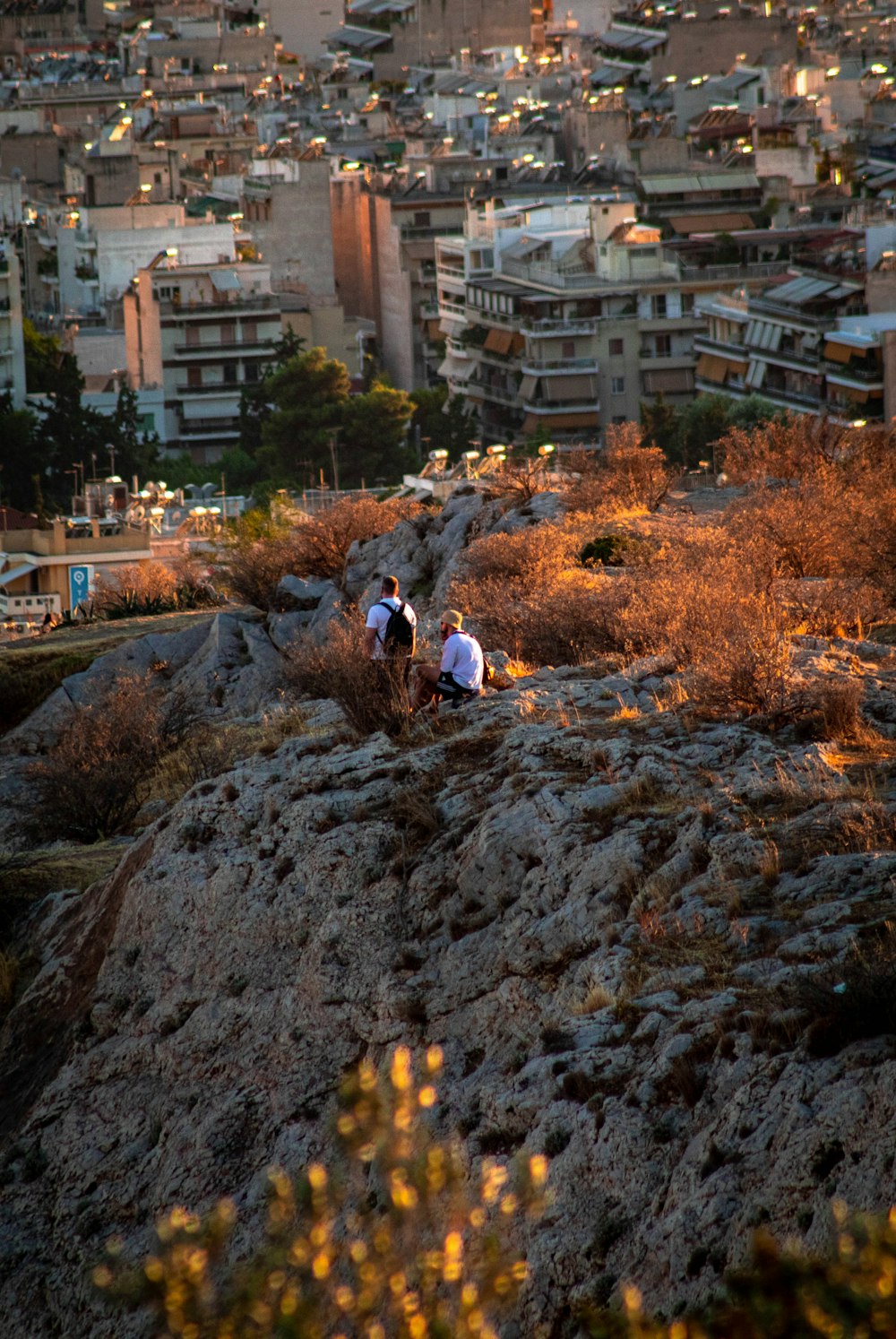 a group of people on a rocky hill with buildings in the background