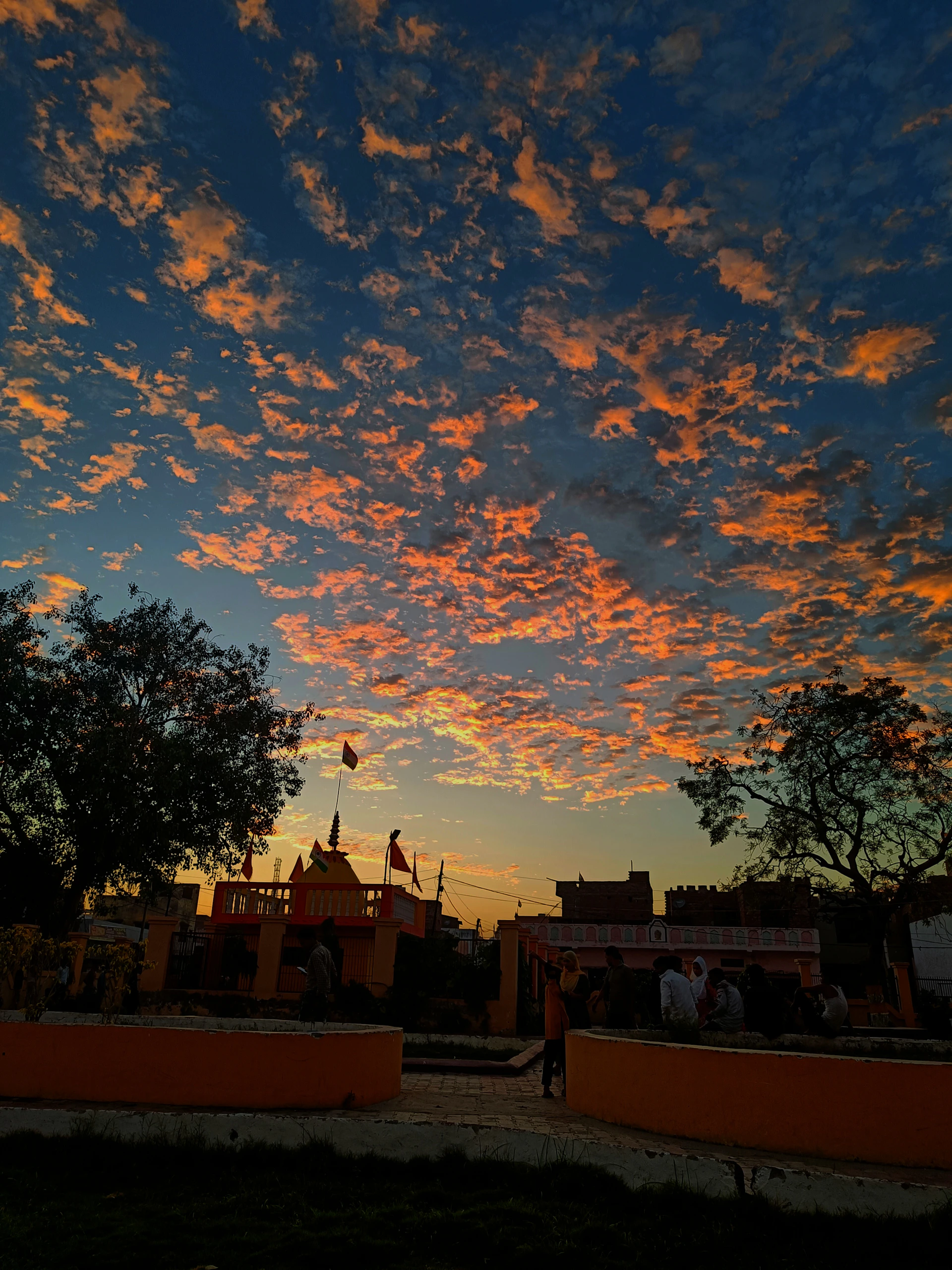 A vibrant photo capturing devotees gathered in deep prayer during a sunset bhakti event, with warm orange hues illuminating the scene.