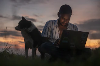 A warm photo of a person smiling while working on a laptop outside at sunrise