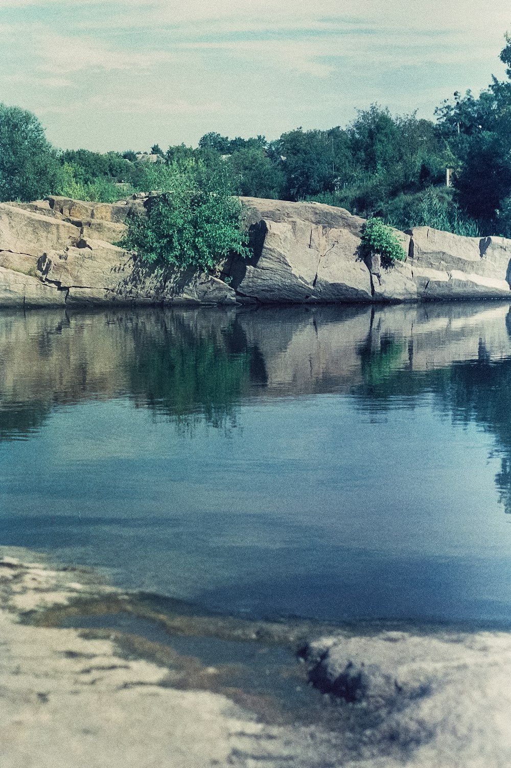 a body of water with a rock cliff and trees on the side