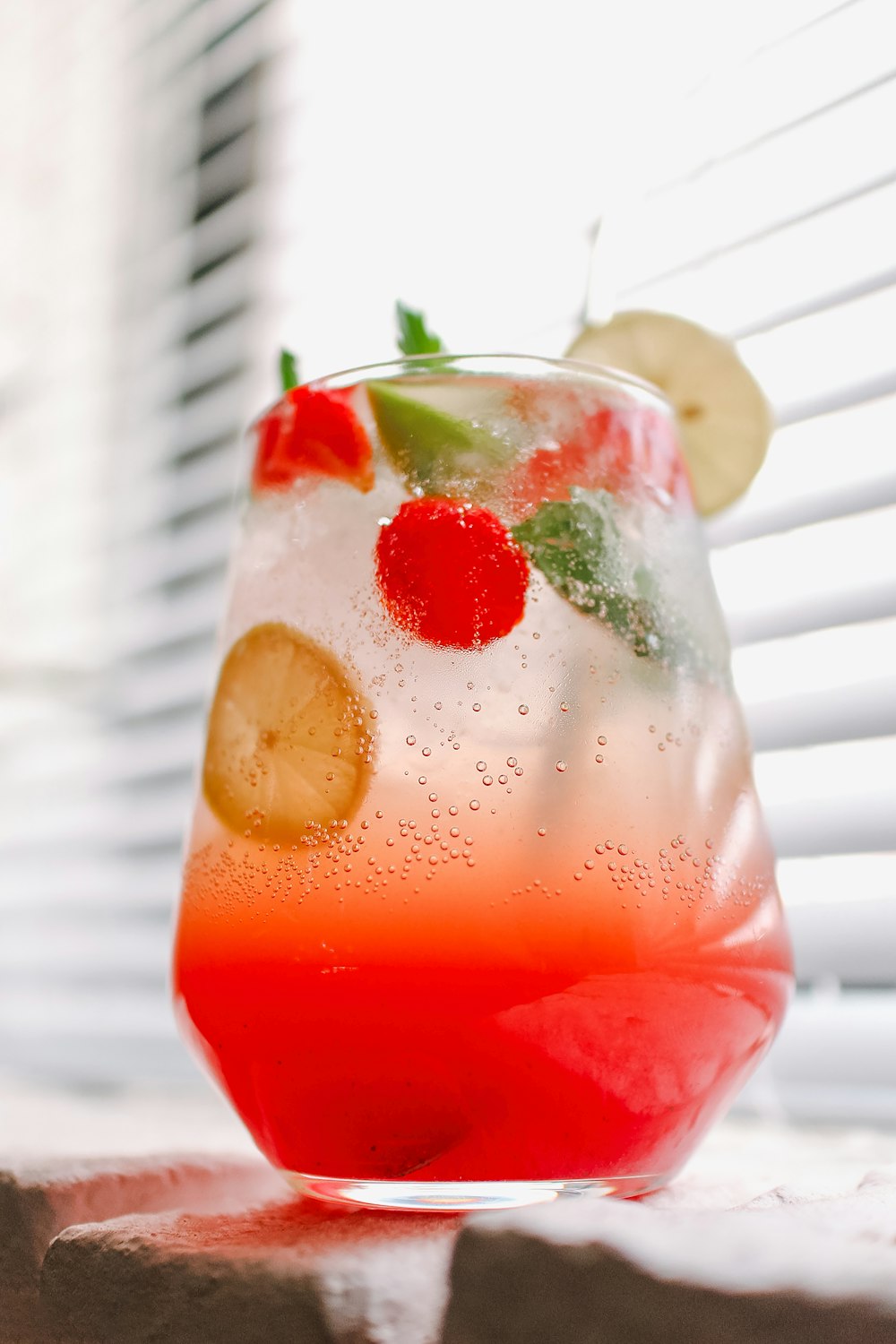 a glass of red liquid with fruit and a straw