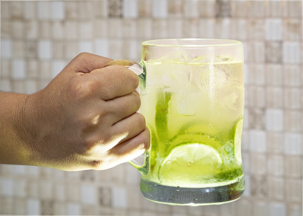 a hand holding a glass of green liquid