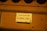 A close-up view of a donation box with a sign in both English and Chinese that reads 'Candle Donation $2'. The sign is placed on a mustard-yellow colored surface.
