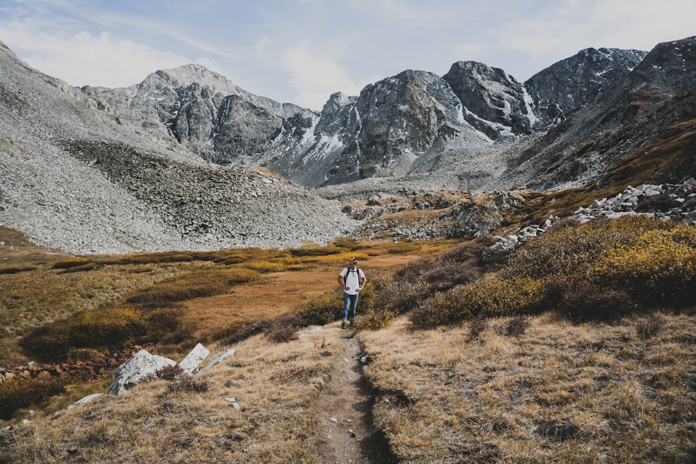 a person walking on a trail in a rocky area with mountains in the background