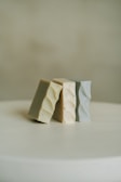 Three rectangular bars of soap are arranged leaning against each other on a plain surface. The soap bars have a textured, wavy pattern on their surfaces and come in different muted colors.