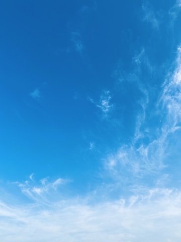 Calm blue sky with wispy clouds over a serene landscape.