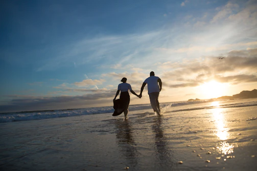 A softly lit photo of a couple holding hands at sunset on a quiet beach.