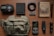 A neatly arranged collection of various items on a wooden surface, including a small first aid pouch, a black elastic band, a book resembling an old newspaper, a tactical pen, a wallet, a multitool, a flashlight, a folding knife, a rugged cellphone, and a green crossbody bag.