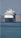 A large, white cruise ship is positioned prominently on the calm sea. The ship is facing the viewer, with its multiple decks and distinctive design clearly visible. In the background, hazy mountains provide a serene backdrop.