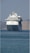 A large, white cruise ship is positioned prominently on the calm sea. The ship is facing the viewer, with its multiple decks and distinctive design clearly visible. In the background, hazy mountains provide a serene backdrop.
