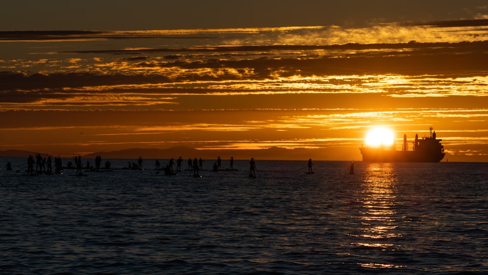 a group of people standing in the water at sunset