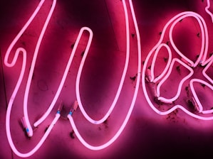 Pink neon lights form an artistic pattern against a dark background, with partially visible wires and connectors adding an industrial feel.
