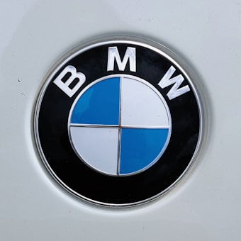 A close-up of the BMW logo featuring a circular emblem with a black outer ring and the letters B, M, and W at the top. The inner circle is divided into four quadrants with alternating blue and white colors.