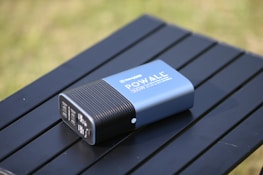 A portable power bank with the label 'POWALL 500W' is placed on a black, slatted table against a blurred outdoor background.