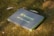 A portable solar charger with the brand name Newpowa and a 40W capacity is resting on grass or moss in a natural outdoor setting. The charger has a handle, suggesting it is designed for easy transport.
