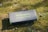 A folded Newpowa 40W solar charger is placed on a grassy surface, with a few scattered pebbles around it. The charger is in a case with a logo and text printed in green.