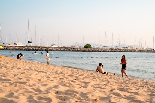 A sunny beach with people enjoying water sports near a marina.