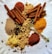 An assortment of spices including cinnamon sticks, ground spices, and various peppercorns is arranged on a white textured surface. A decorative golden spoon is also present among the spices.