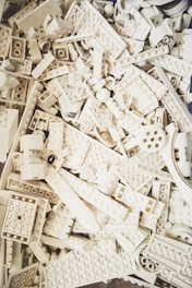 A collection of white plastic building blocks, resembling LEGO pieces, stacked and scattered in various shapes and sizes.