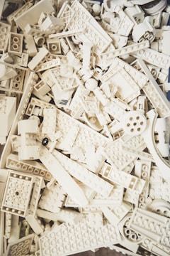 A collection of white plastic building blocks, resembling LEGO pieces, stacked and scattered in various shapes and sizes.