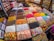 A vibrant market stall displaying an array of colorful candies and sweets in bins and trays. The sweets include various shapes and textures such as gummy bears, striped lollipops, and chocolate-coated treats, all neatly organized in individual sections.