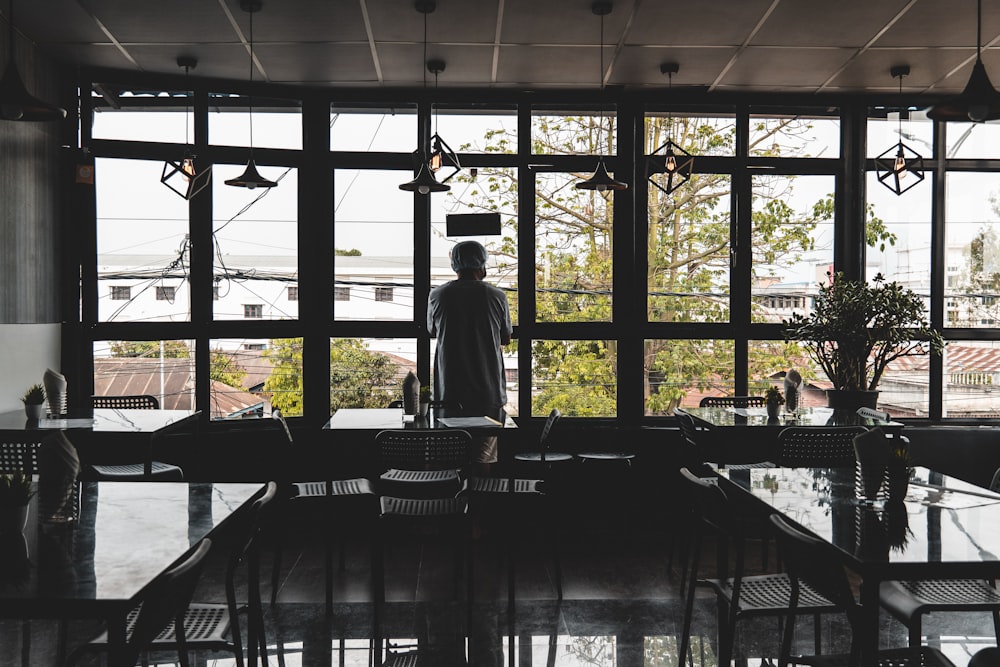 a person standing in a room with large windows and tables