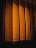 Patterned curtains illuminated by a warm light, casting shadows that create a sense of depth and texture.