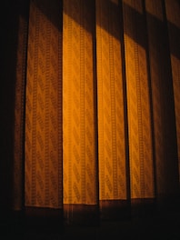 Patterned curtains illuminated by a warm light, casting shadows that create a sense of depth and texture.