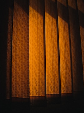 Patterned curtains illuminated by a warm light, casting shadows that create a sense of depth and texture.