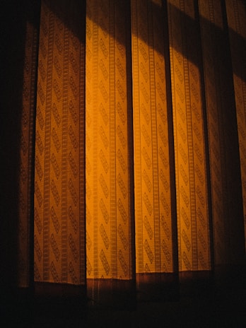 Patterned curtains illuminated by a warm light, casting shadows that create a sense of depth and texture.