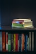 A collection of self-help and motivational books are neatly organized on a black bookshelf. On the top shelf, there is a small stack of books including 'Tuesdays with Morrie', 'The Magic of Thinking Big', 'Think and Grow Rich', and 'The Power of Now'. The bottom shelf displays a variety of books such as 'The Alchemist', 'Freedom from the Known', and 'The 7 Habits of Highly Effective People'. The setup suggests a personal library focused on personal development.