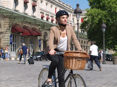 Woman riding bicycle with basket in front of building