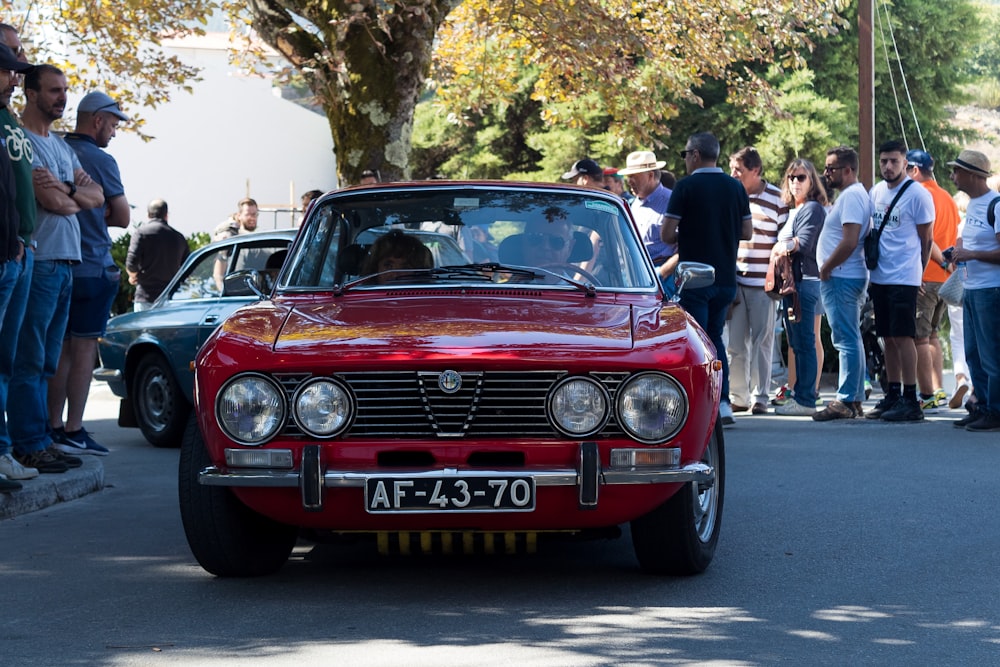 a group of people looking at a red car