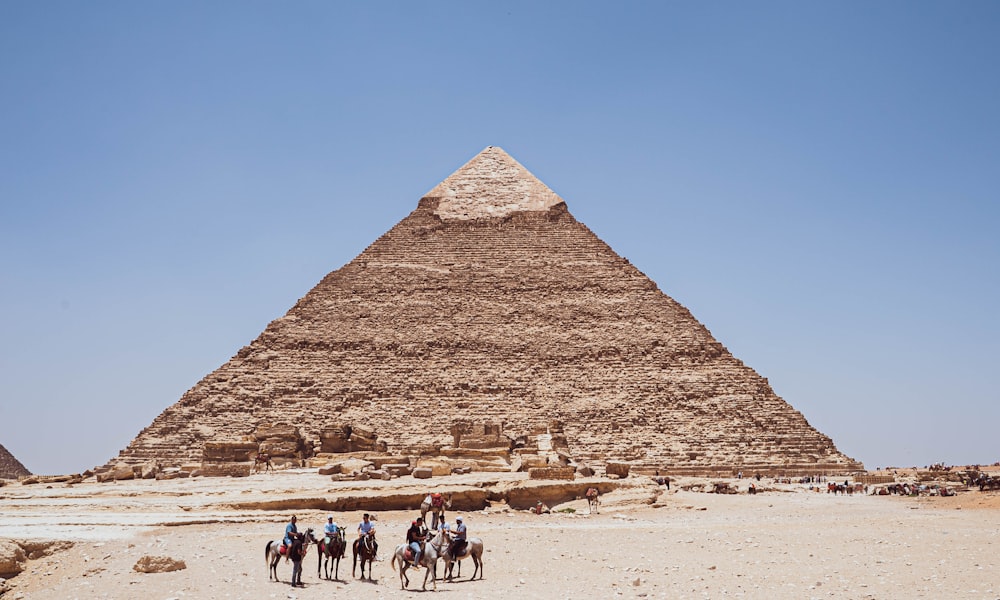 Un grupo de personas montando camellos frente a una pirámide